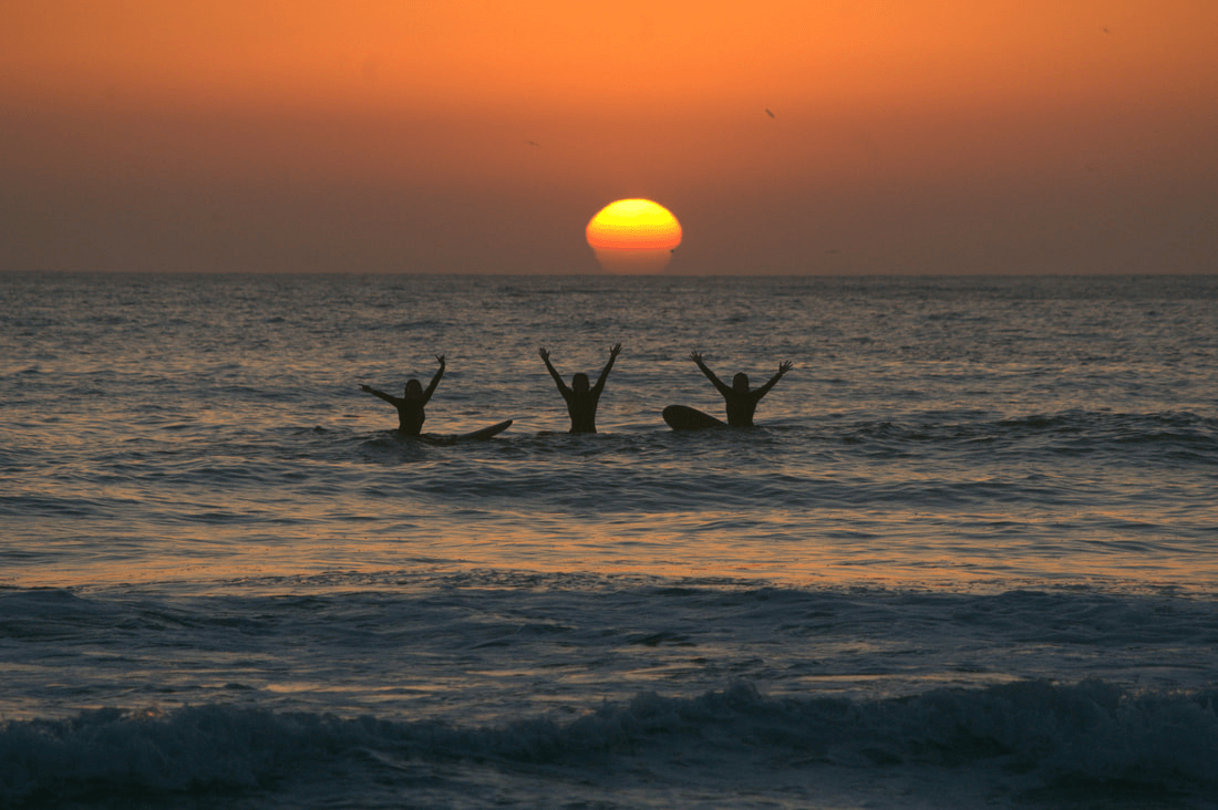 Female surfers waving from the ocean at sunset in Taghazout