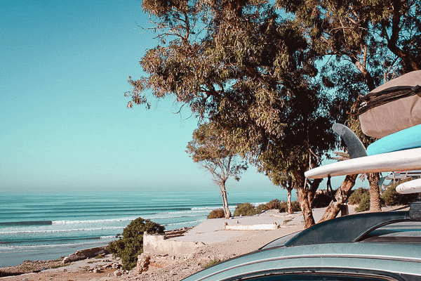 Surf boards on the roof of a car in front of the beach in Taghazout